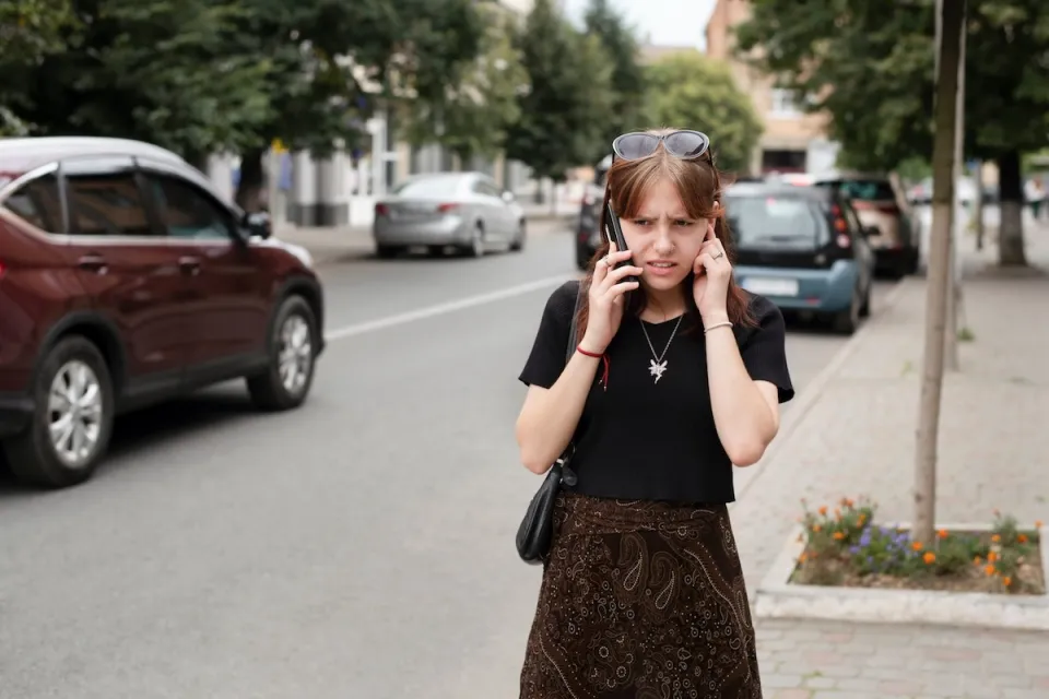 Girl on phone struggling to hear standing on loud city street.